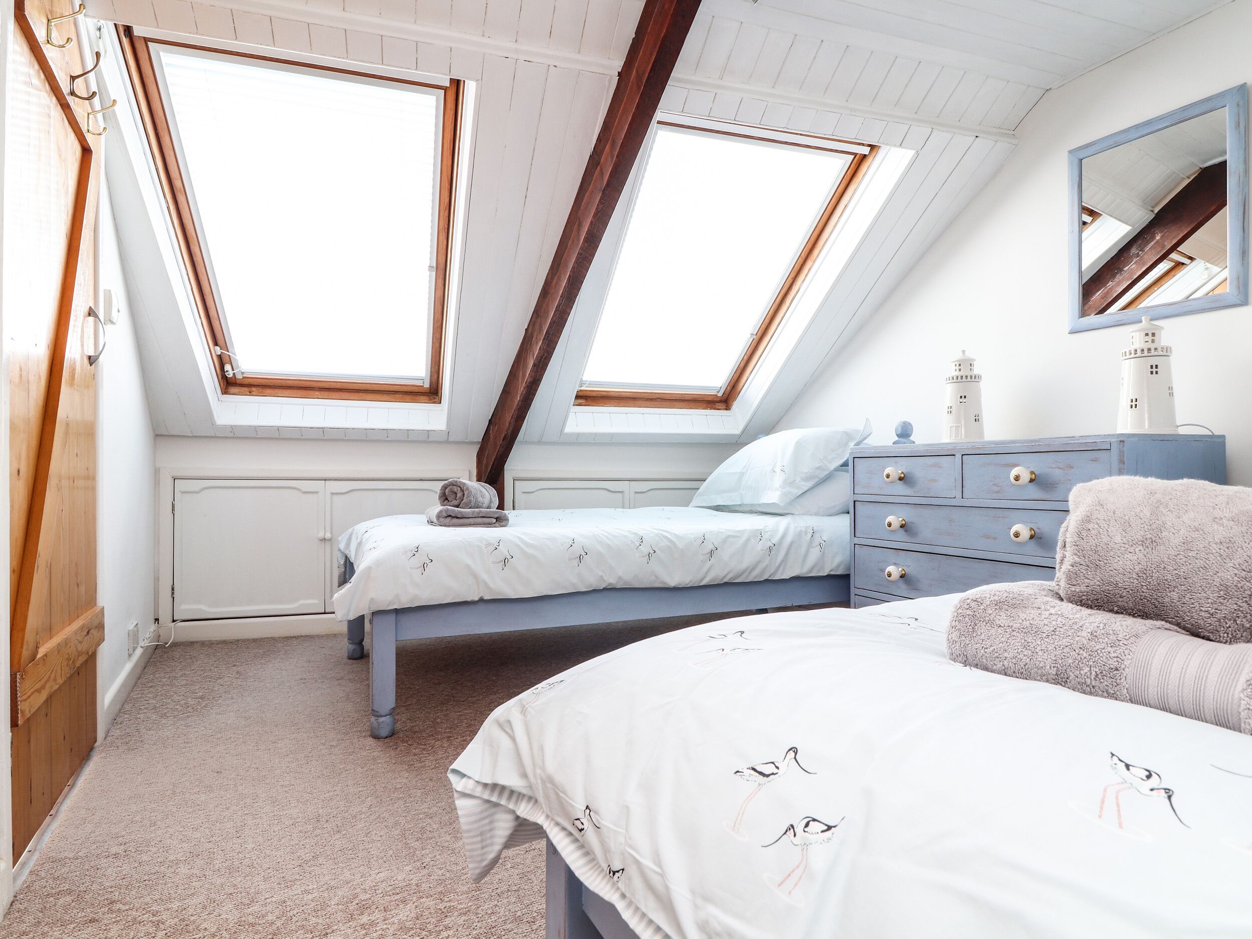 Een slaapkamer met twee bedden, een dressoir en een spiegel. Er zijn dakramen en uitzicht op buiten.