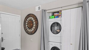 Un lavadero con lavadora y secadora empotradas, una puerta con perchero y una pieza decorativa en la pared con forma de sol.