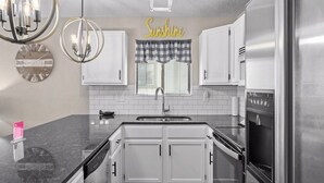 Una cocina moderna con armarios blancos, un refrigerador de acero inoxidable, horno empotrado y una lámpara colgante.