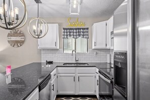 A modern kitchen with white cabinets, a stainless steel refrigerator, a built-in oven, and a pendant light fixture.