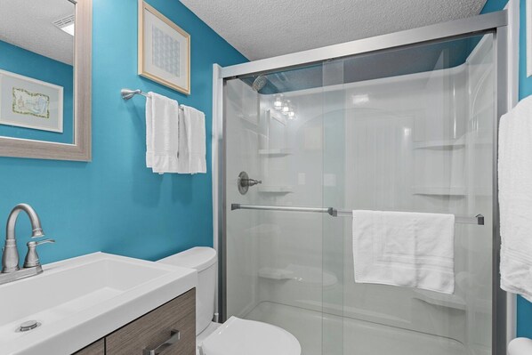 A bathroom with a glass-enclosed shower, a white sink, and a toilet.