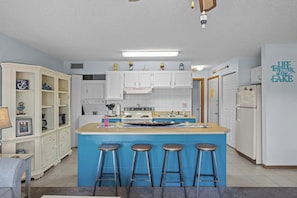 Una cocina con una isla central, taburetes de bar, armarios blancos, un refrigerador y una pared con una cita inspiradora.