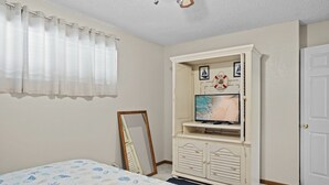 A bedroom with a bed, a TV on a dresser, a mirror, and a door.