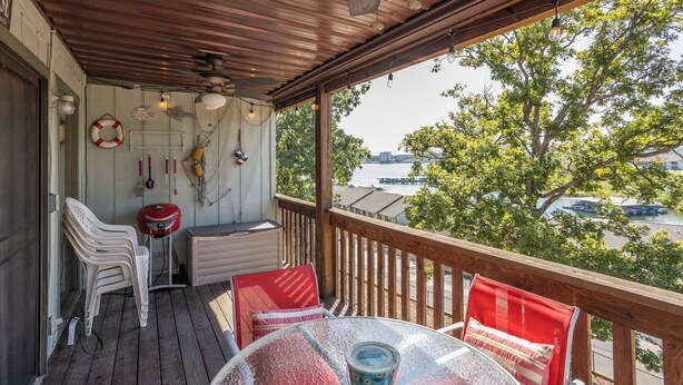 A covered outdoor area with a table and chairs, a ceiling fan, and a view of a body of water with boats.