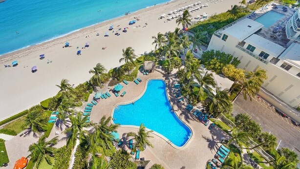Vista aérea de un resort con piscina, playa y palmeras.