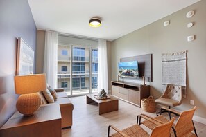 Un salon moderne doté d’un téléviseur à écran plat, d’un ensemble de canapés, d’une table basse et d’une grande fenêtre offrant une vue sur les bâtiments.