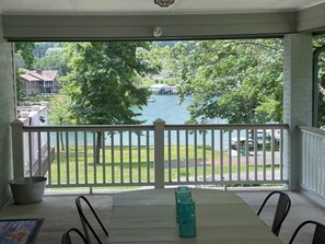 Een overdekt terras met een tafel en stoelen, met uitzicht op een meer en een witte balustrade.