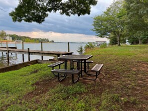 Ein Picknicktisch mit Bänken am See, umgeben von Gras und Bäumen.