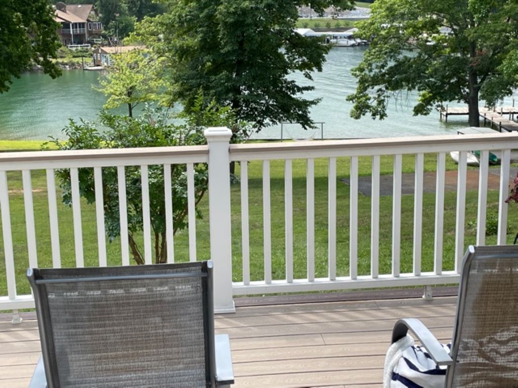 Une terrasse avec des rampes blanches donnant sur un lac, agrémentée de chaises et d’une table.