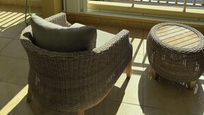 Un balcón con muebles de mimbre, vista a un puerto deportivo y una noria al fondo.