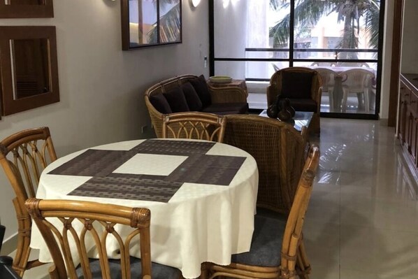 A dining area with a round table covered by a white tablecloth, surrounded by wicker chairs.