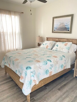 A bedroom with a wooden bed, floral bedding, a ceiling fan, a nightstand with a lamp, and a framed picture on the wall. - Hidden Lake Condos on 30A, 6min walk to Gulfview Heights beach access, pool, gym (Santa Rosa Beach)