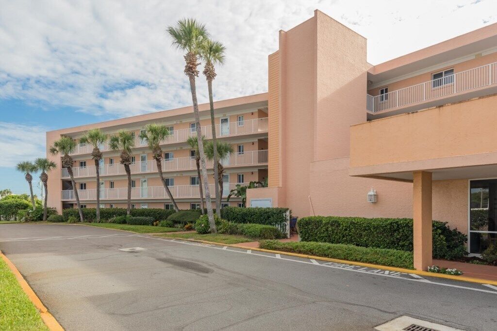 A multi-story hotel with balconies, palm trees, and a clear sky.