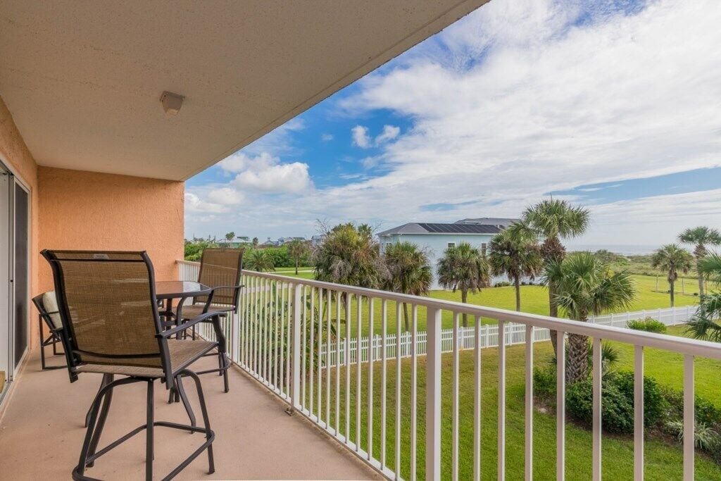 A balcony with outdoor furniture, a white railing, and a view of a golf course with palm trees.