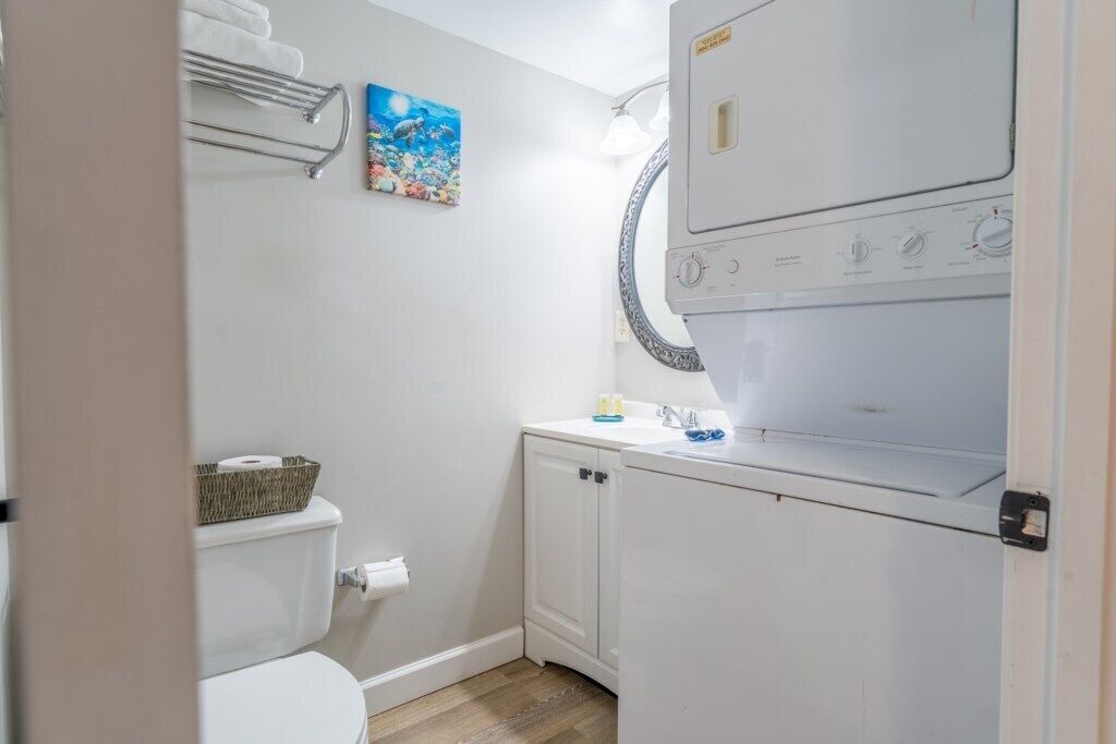A compact laundry room with a washing machine, a sink, and a toilet.