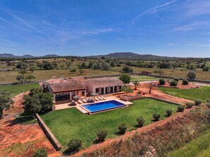 Uma vila com piscina, cercada por um gramado bem cuidado e vista para colinas distantes.