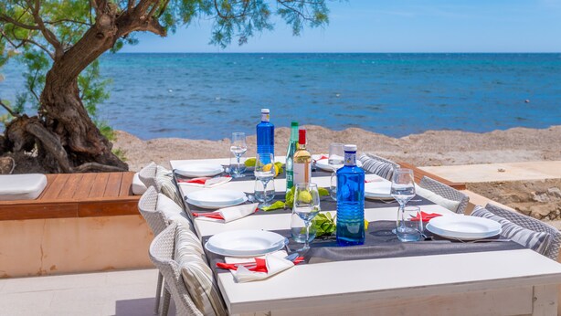 A table set for two with a view of the sea, a bottle of water, and a bottle of wine. - CAS FERRERICO - Cozy summer house on the beachfront. Free WIFI. (Cala Bona)