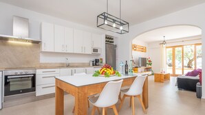 A modern kitchen with white cabinets, a wooden dining table, and a built-in oven. - CAS FERRERICO - Cozy summer house on the beachfront. Free WIFI. (Cala Bona)