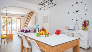 A modern kitchen with a wooden table, white chairs, and a fruit bowl on the counter. - CAS FERRERICO - Cozy summer house on the beachfront. Free WIFI. (Cala Bona)