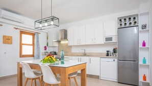 A modern kitchen with white cabinets, a stainless steel refrigerator, and a wooden dining table with chairs. - CAS FERRERICO - Cozy summer house on the beachfront. Free WIFI. (Cala Bona)