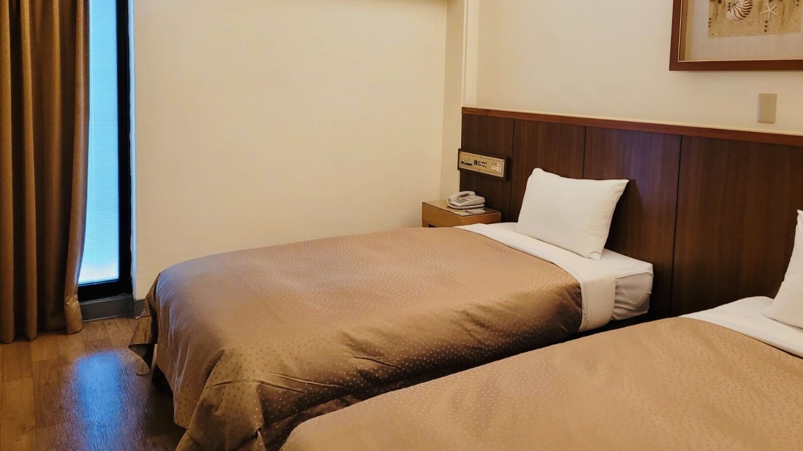 A hotel room with two beds, a wooden headboard, a nightstand, and a framed picture on the wall.