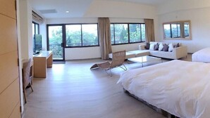 A spacious hotel room with a large bed, a sofa, a dining table, and a chair. There are large windows providing a view of the outdoors. - Dongxu Resort Hotel (Hualien City)