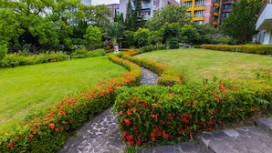 A landscaped garden with a stone pathway, surrounded by green grass and red flowers, with multi-story residential buildings in the background. - Dongxu Resort Hotel (Hualien City)