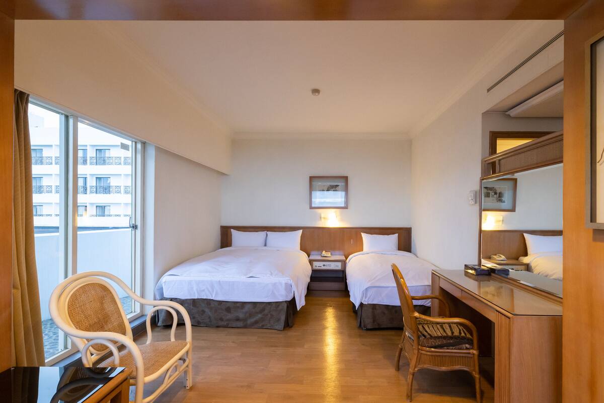 Een hotelkamer met twee bedden, een bureau, een stoel en een groot raam.