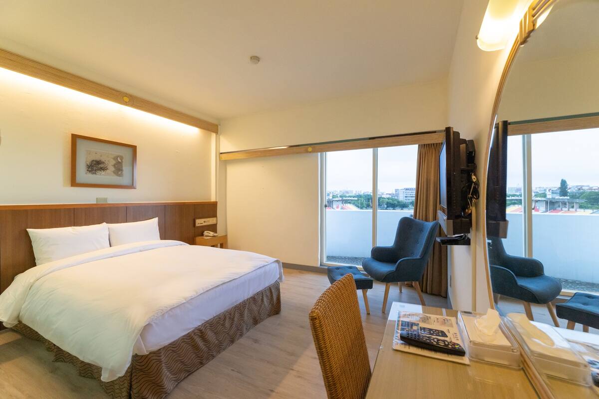 Hotelkamer met een groot bed, bureau met stoel, televisie en raam met uitzicht op de stad.