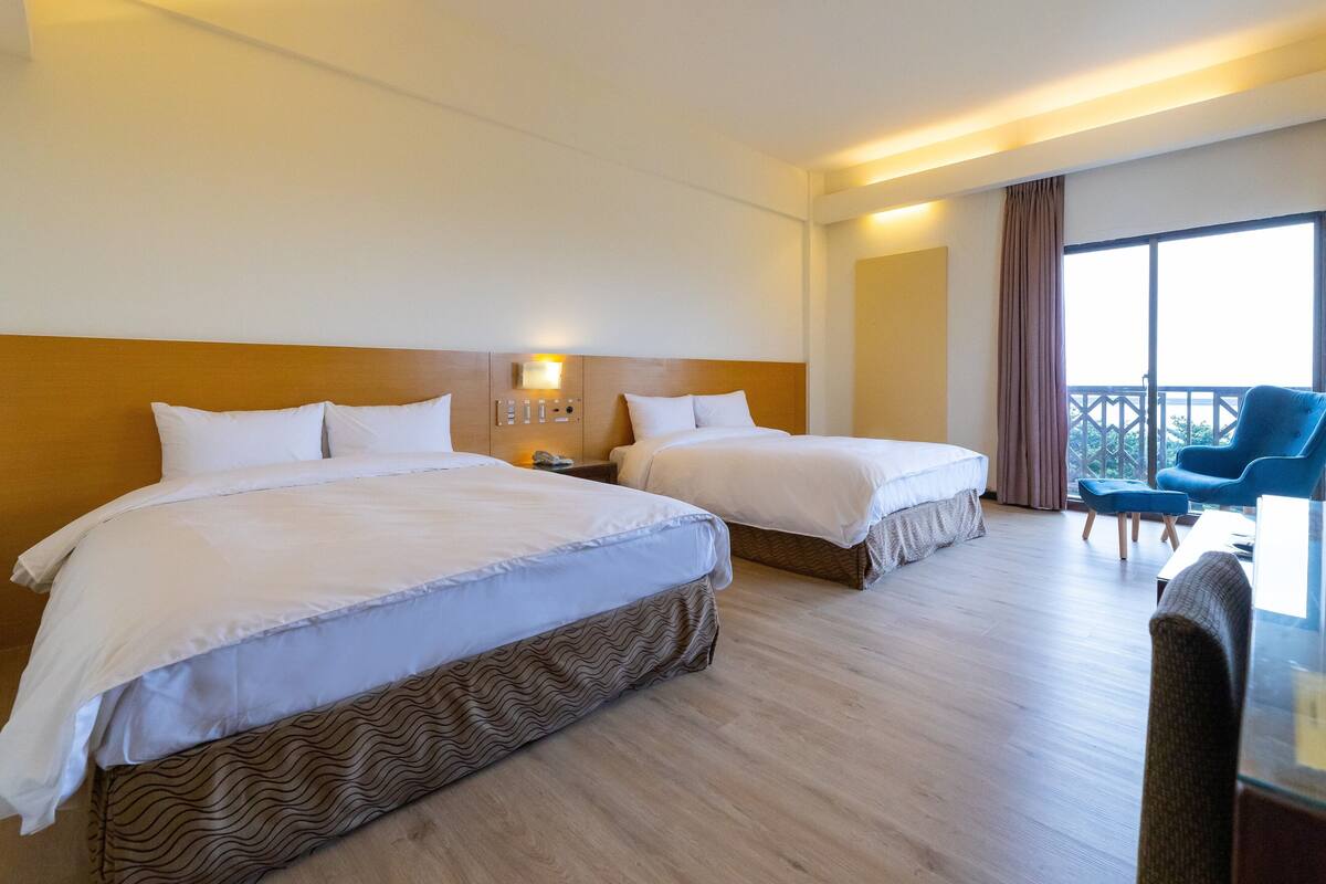 Een hotelkamer met twee bedden, een bureau, een stoel en een balkon met uitzicht.