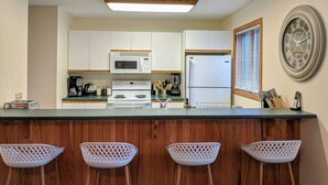 Una cocina con armarios blancos, microondas, estufa, refrigerador y un reloj en la pared.