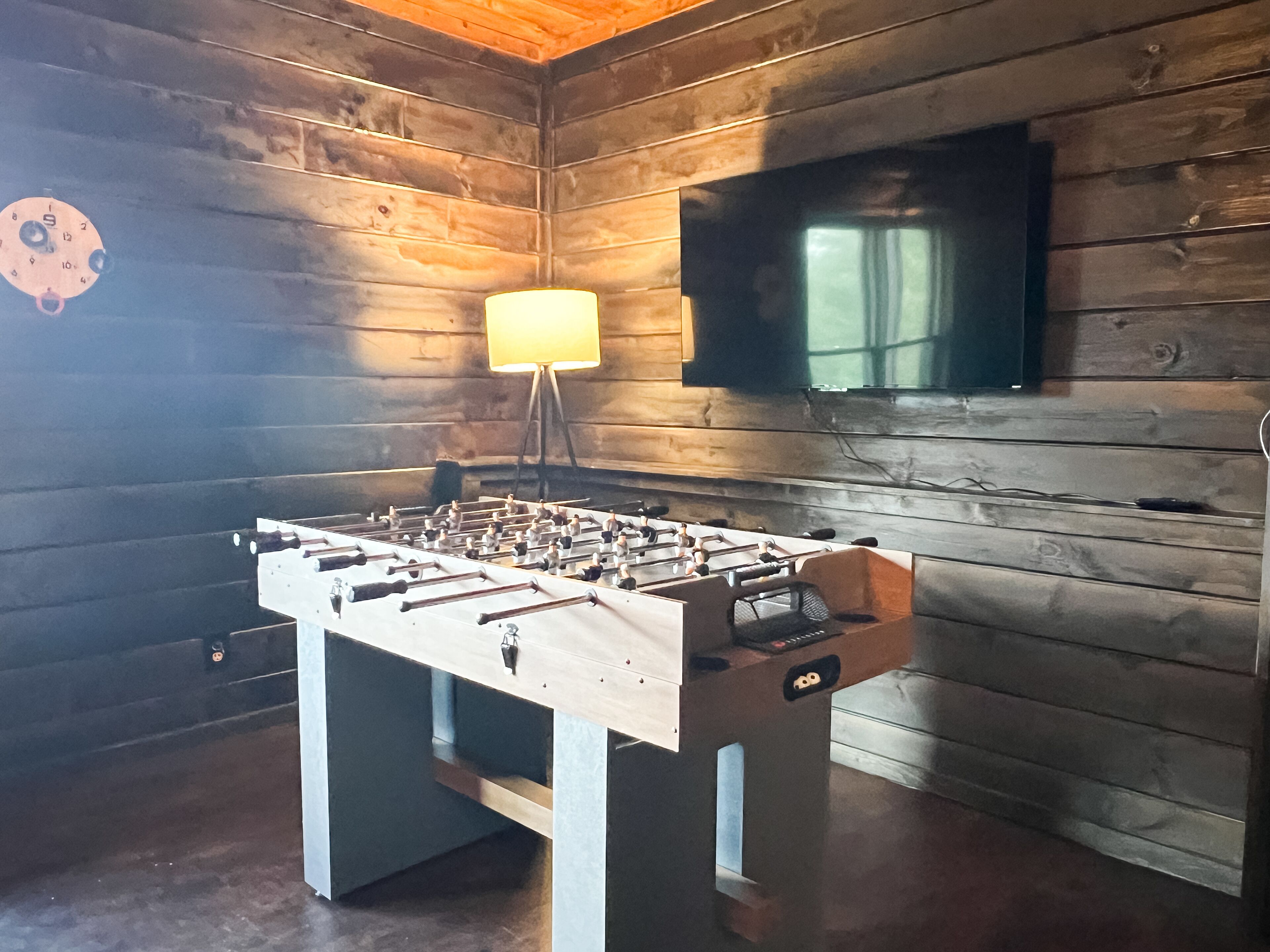 A wooden-floored room with a foosball table, a TV mounted on the wall, and a lamp.