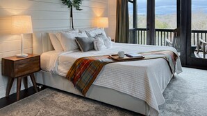 Une chambre à coucher avec un lit, des tables de chevet, une fenêtre avec des rideaux et une vue sur l’extérieur.