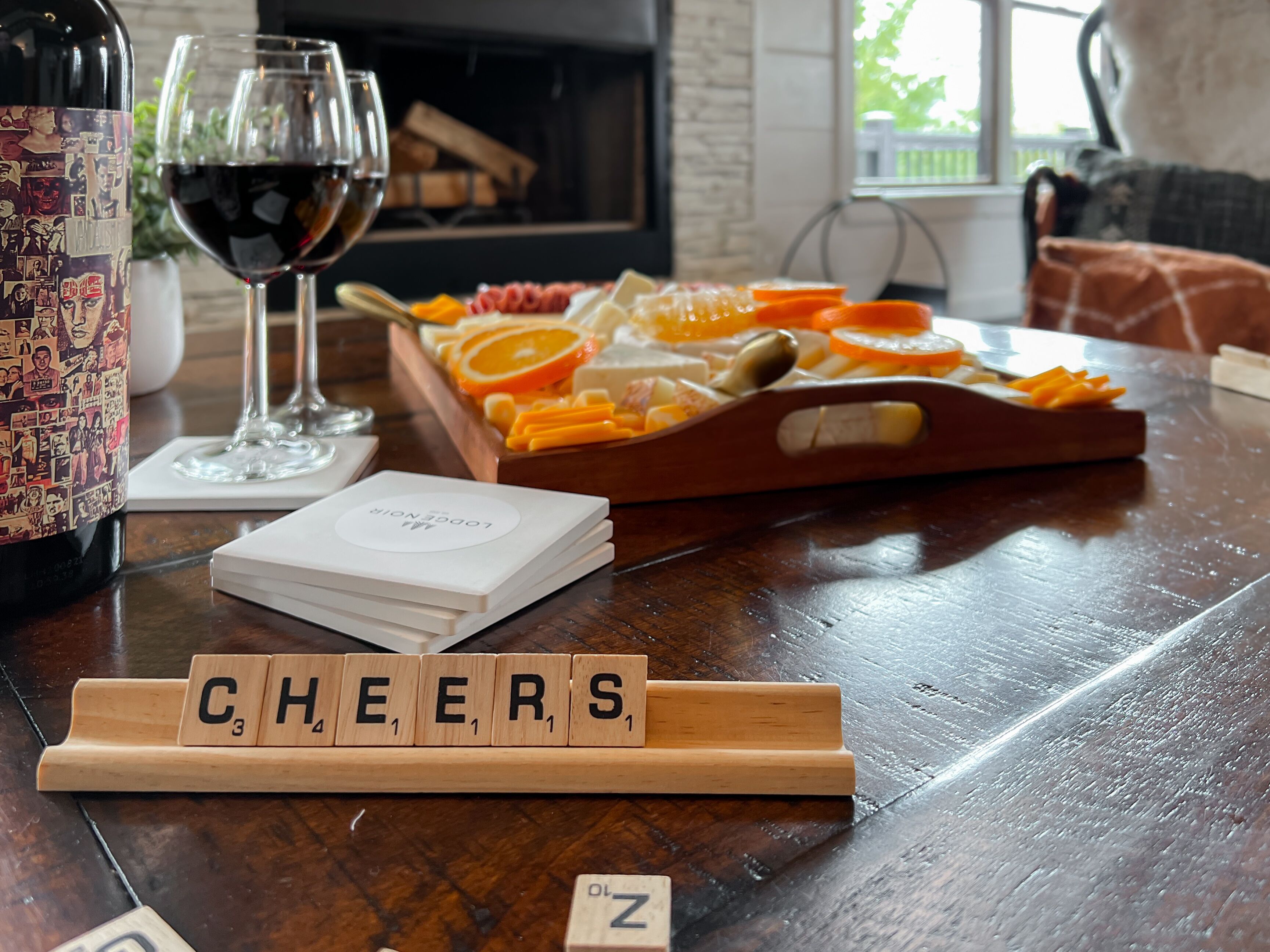 A wooden tray with sliced oranges and cheese, a bottle of wine, and a glass of red wine on a wooden table.