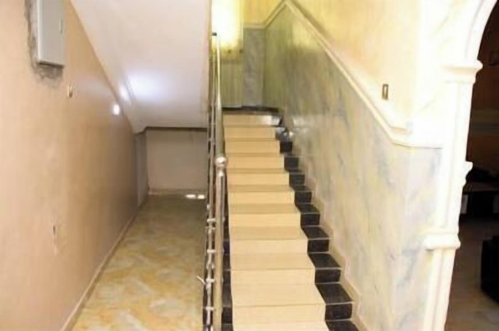 A staircase with a handrail, marble walls, and a tiled floor.