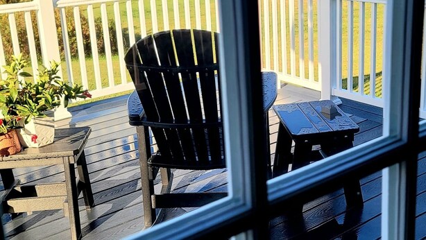 A wooden deck with a view of a waterfront, featuring a white railing, a black Adirondack chair, and a small table. - Spectacular Corea Harbor side Home minutes to Acadia National Park Schoodic Gate (Gouldsboro)