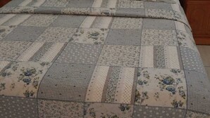 Una cama con colcha estampada, mesitas de noche de madera y un ventanal con persianas.