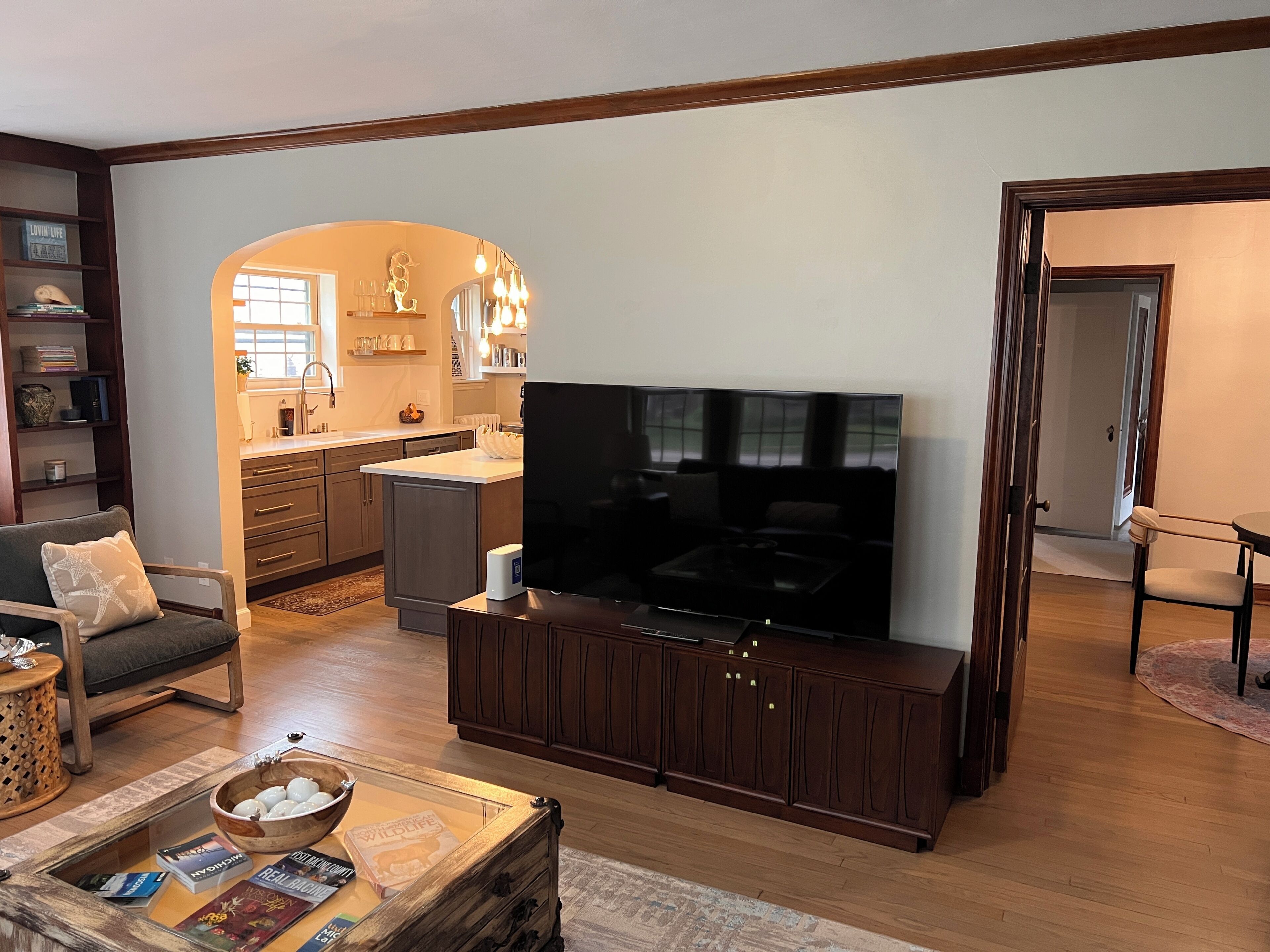 Una sala de estar con televisor, armarios de madera, un sofá y una cocina al fondo.