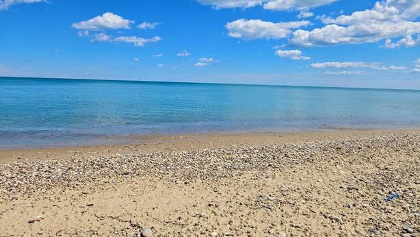 Een strand met kiezels en een helderblauwe lucht.