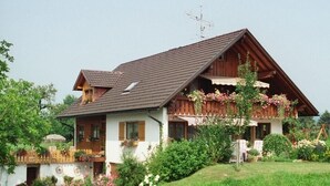 Un chalet traditionnel doté d’un toit à pente, de balcons en bois et d’un jardin agrémenté de fleurs et d’arbustes.