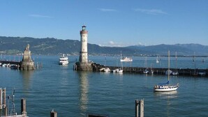 Un phare, une jetée et des bateaux dans un port, avec des montagnes en arrière-plan.