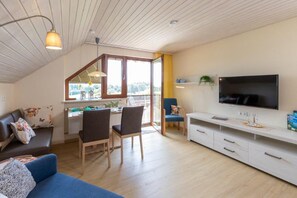 A cozy living room with a sofa, chairs, a TV, and a dining area with a window.