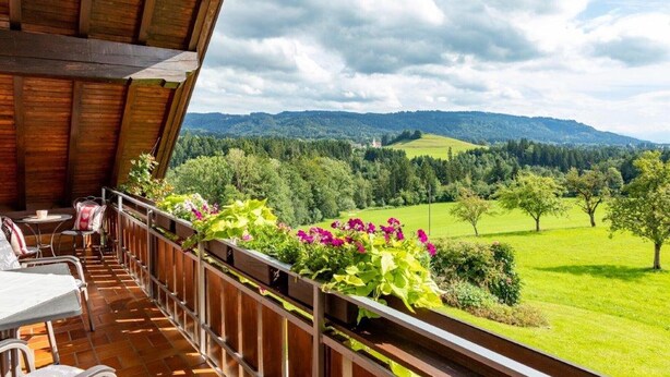 Un balcon offrant une vue sur un paysage verdoyant et des collines lointaines.