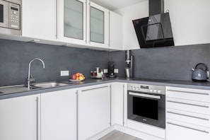 A modern kitchen with white cabinets, a built-in oven, a coffee maker, and a kettle on the counter.