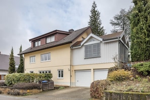 A two-story residential building with a garage, a sloped roof, and a small garden area.