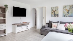 A modern living room with a flat-screen TV, a grey sofa with decorative pillows, a wooden sideboard, and two wall-mounted paintings. - Pet-Friendly Apartment Holly with Wi-Fi & Terrace (Ebringen)