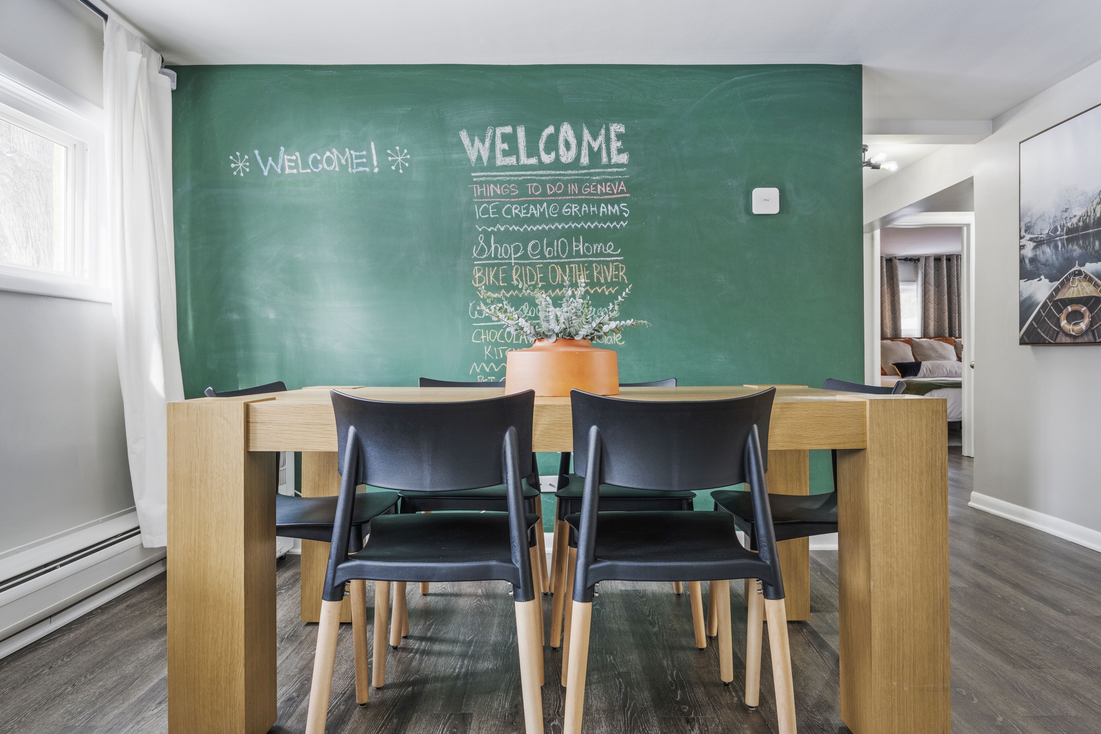 Un coin repas avec un mur recouvert d’un tableau noir où sont énumérées les activités proposées à Genève, une table en bois et des chaises noires.
