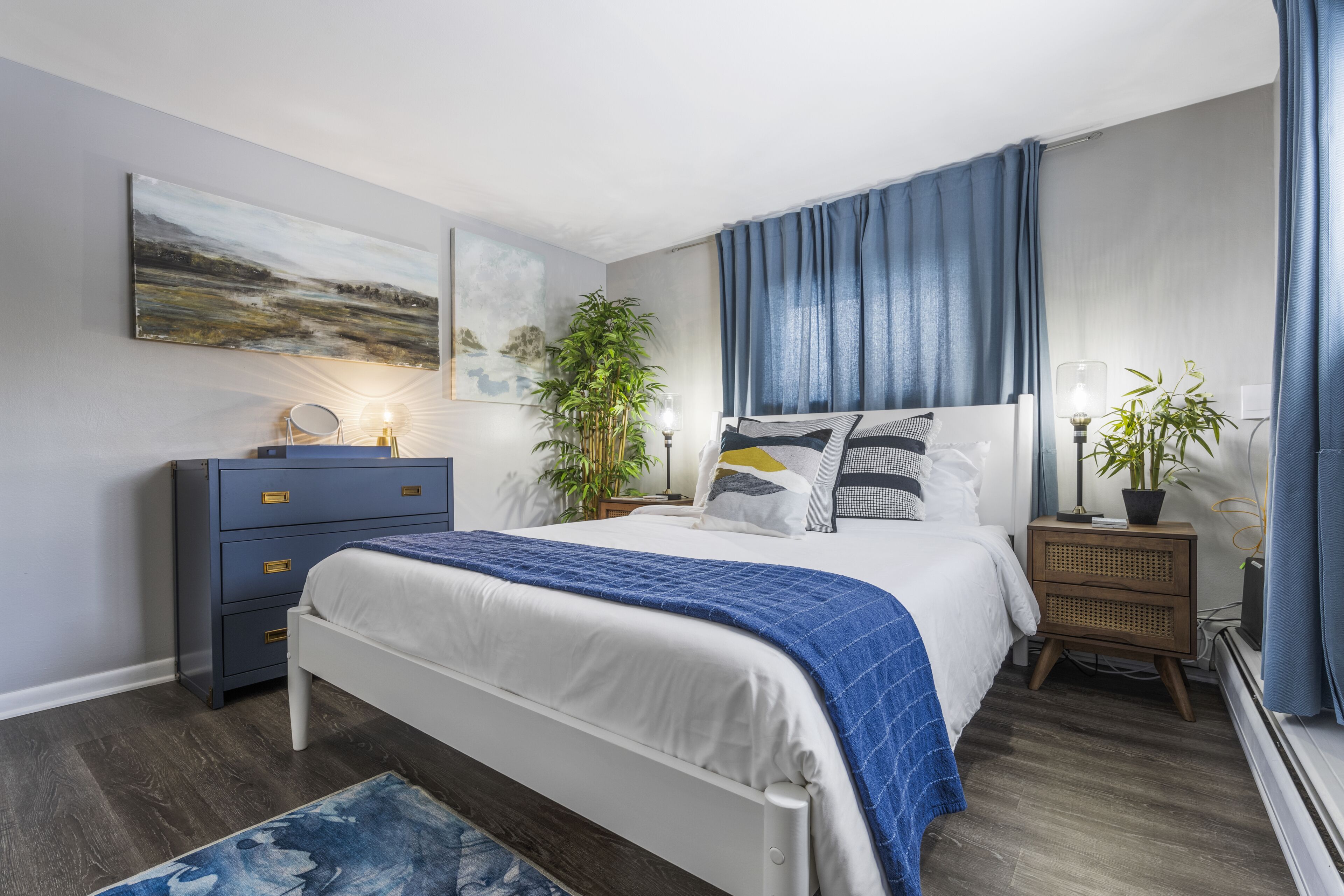 A modern bedroom with a bed, bedside tables, a dresser, and a large window with curtains.