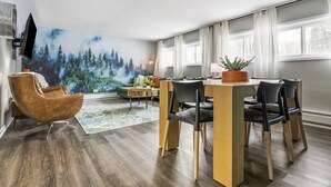 Un'area pranzo moderna con un tavolo e sedie in legno, un murale raffigurante una foresta sulla parete e un'ampia finestra che offre luce naturale.