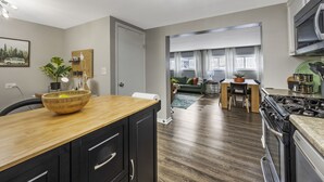 Una cucina moderna con un piano di lavoro in legno, mobili neri e un piano cottura. C'è una zona pranzo con tavolo e sedie, e un soggiorno con divano e tavolino.